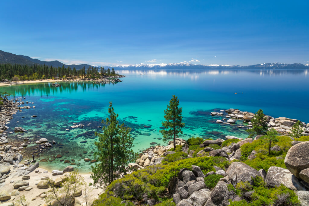 Turquoise waters of Lake Tahoe with view over snowy peaks of Sierra Nevada mountains