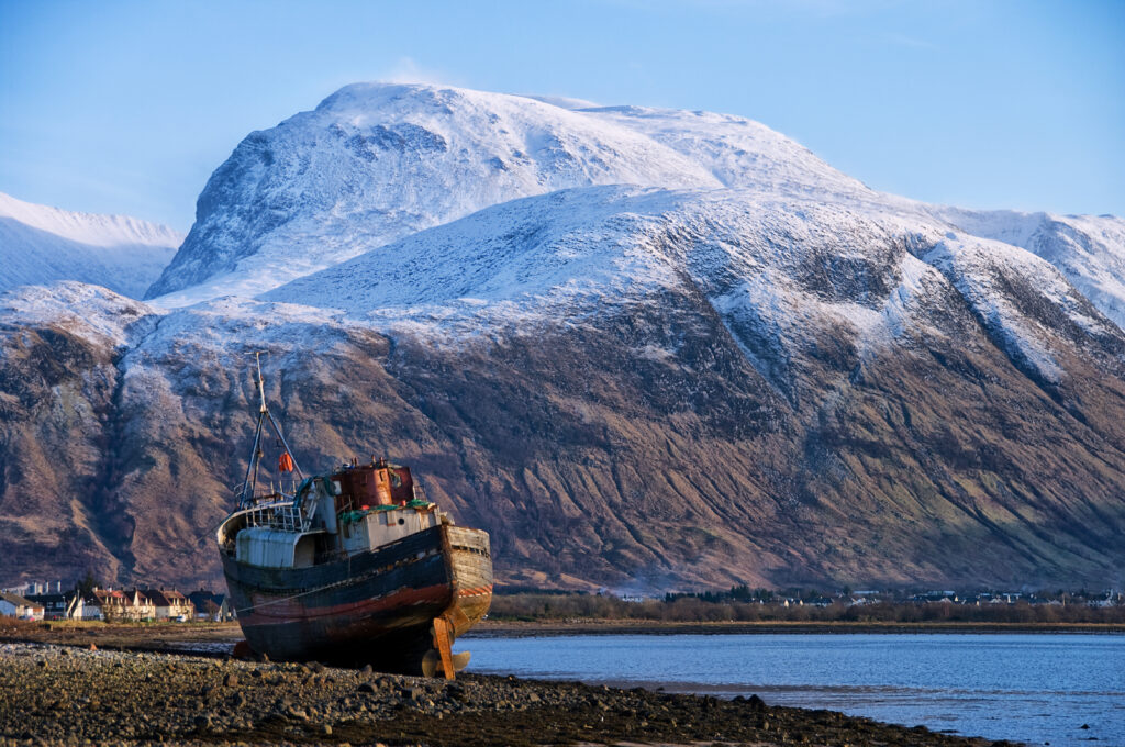 Ben Nevis Scotland. Snow on Ben Nevis with an old fishing trawler on the beach at Corpach in the foreground