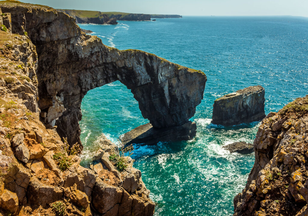 The Green Bridge of Wales with lichen-covered rocks in the foreground on the Pembrokeshire coast, near Castlemartin in early summer