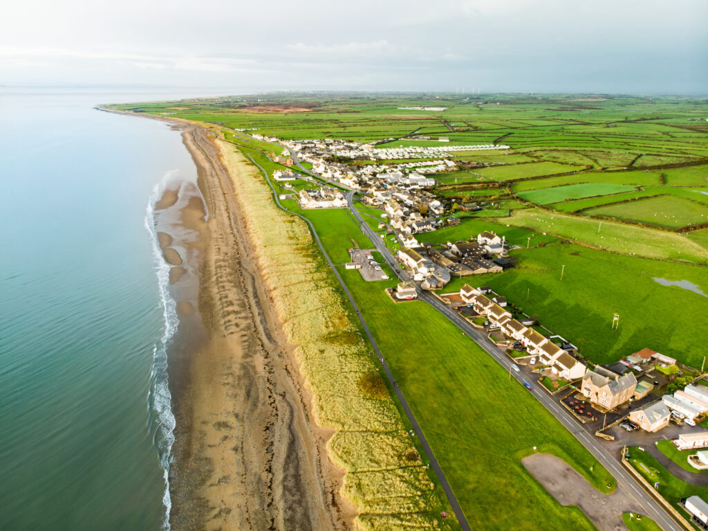 Aerial view of Allonby village beach in Allerdale district in Cumbria, UK. Pebble shore of Allonby bay and endless green pastures on autumn evening.