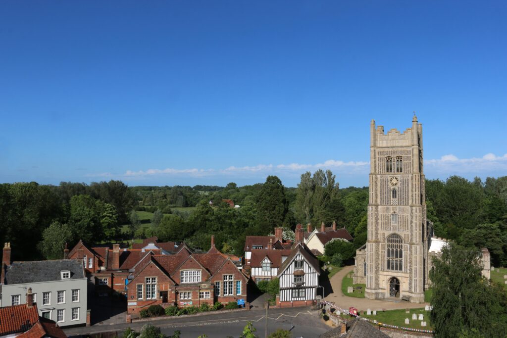 Eye parish church of Saint Peter and Saint Paul in Suffolk with buildings, trees and blue sky with white cloud in the background.