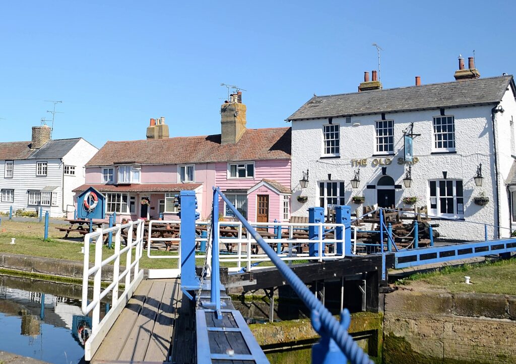 A scenic view of a canal lock, leading to a traditional English pub and pink house in Heybridge Basin, Essex, England