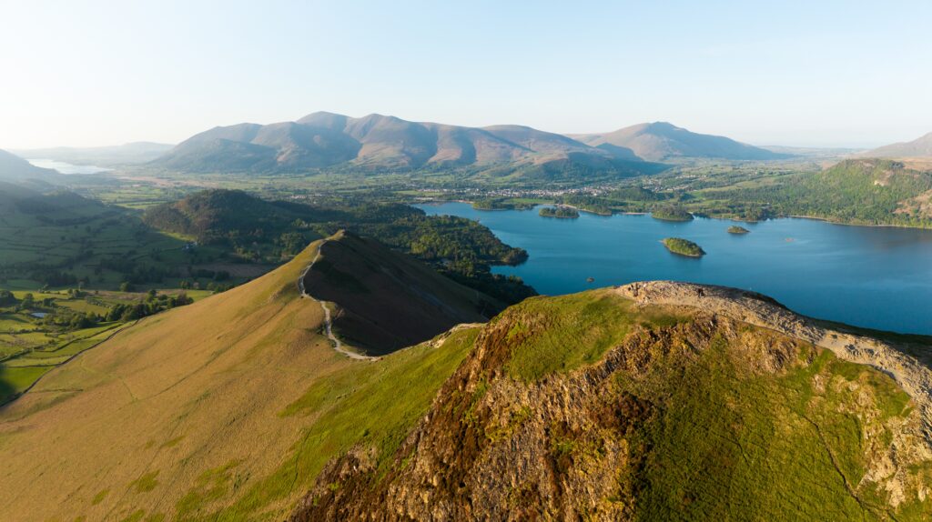 Aerial panorama landscape of the walking path along Catbells mountain ridge in the English Lake District National Park with Derwent Water lake and Keswick town below the Northern Fells on a sunny day
