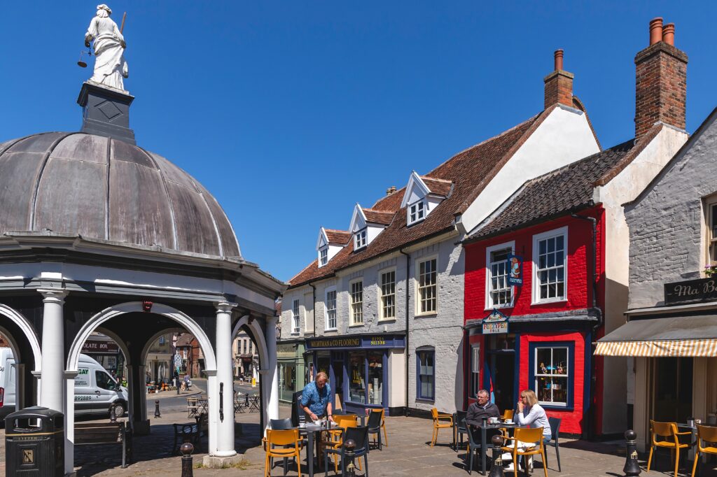 People relaxing at tables set up on the market square, by the Butter Cross, on a wonderfully sunny and warm day in the market town of Bungay.