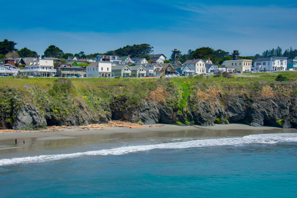 The seacoast village of Mendocino, California lines an ocean headland at low tide on a sunny spring afternoon.