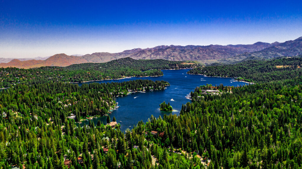Aerial, drone panorama of Lake Arrowhead in the San Bernardino Mountains, California on a clear, summer day with blue water and sky, purple mountains and green trees