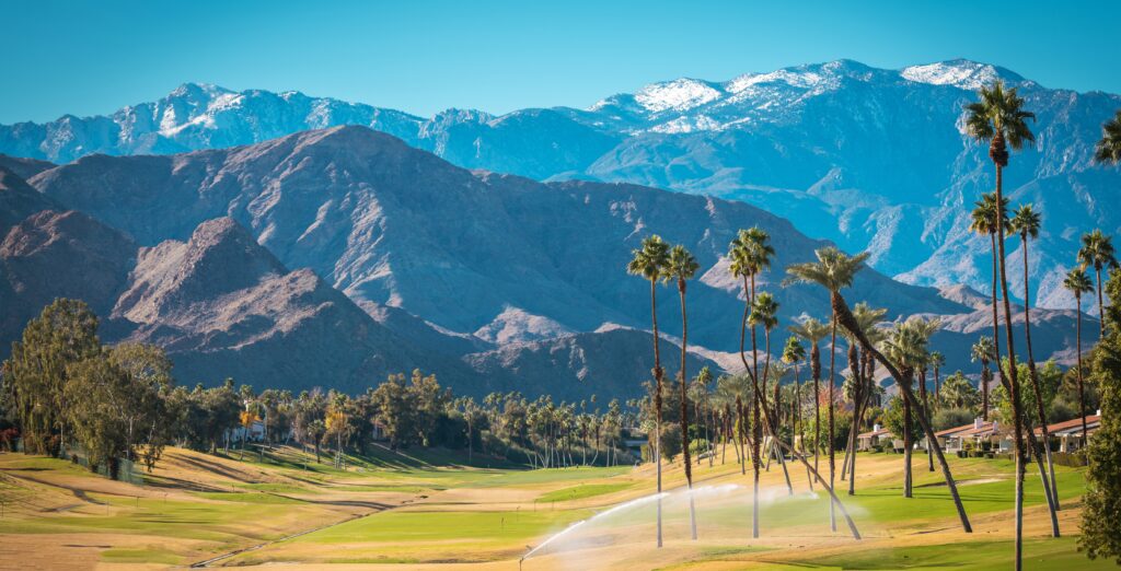 Sunny Warm Winter Time in the Palm Desert Coachella Valley. Golf Courses, Palms and Mountains Covered by Fresh Snow. Recreation in Southern California State, United States of America.