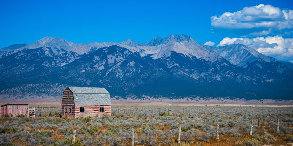 Sangre de Cristo Mountains and arid wilderness meadow with red barns in Alamosa, Colorado, USA