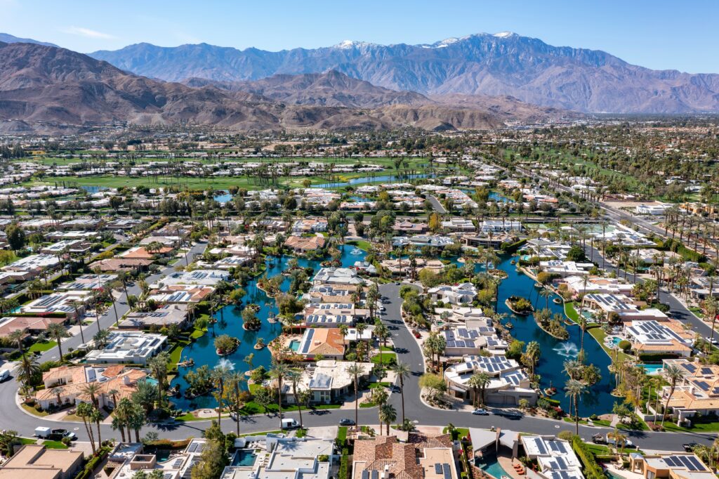 Aerial view of a beautiful and upscale community in the Rancho Mirage area of Palm Springs, California with palm trees and golf courses with the San Bernardino Mountains in the distance.