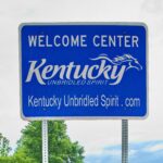 Kentucky Welcome Center highway sign featuring the state slogan Kentucky Unbridled Spirit against a cloudy sky and green trees, symbolizing travel and tourism.