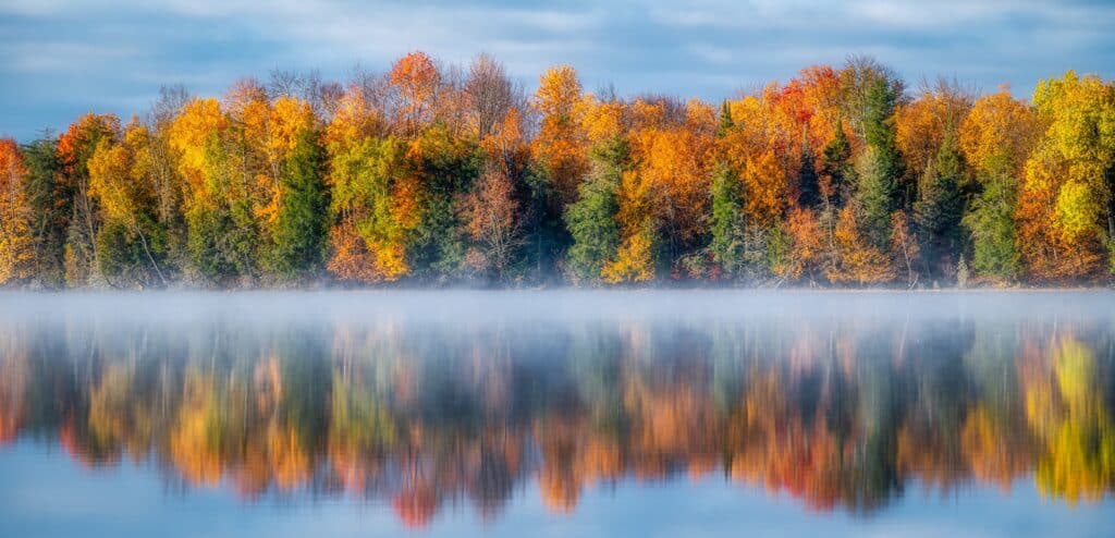 Beautiful fall colors reflected in the water of a northern Wisconsin lake with an early morning mist hovering over the water.