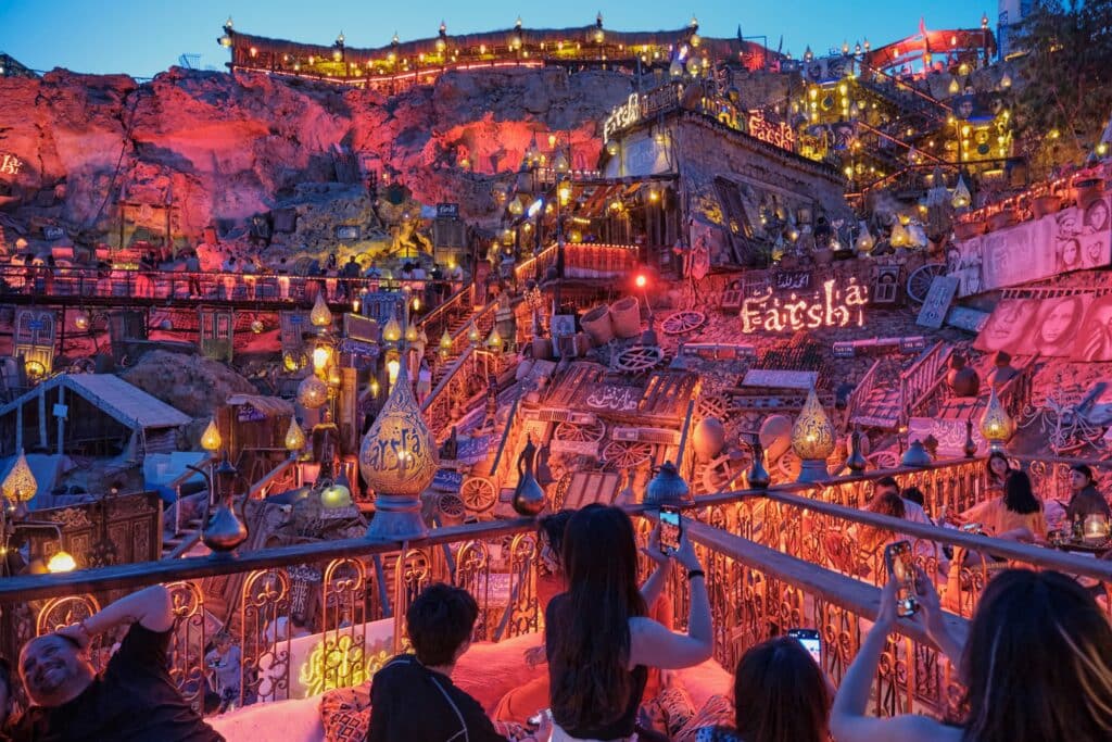 Sharm El Sheikh, Egypt: Vibrant hillside cafe Farsha at twilight, illuminated by warm, decorative lights and traditional ornaments, visitors enjoying view. Scenic cultural ambiance