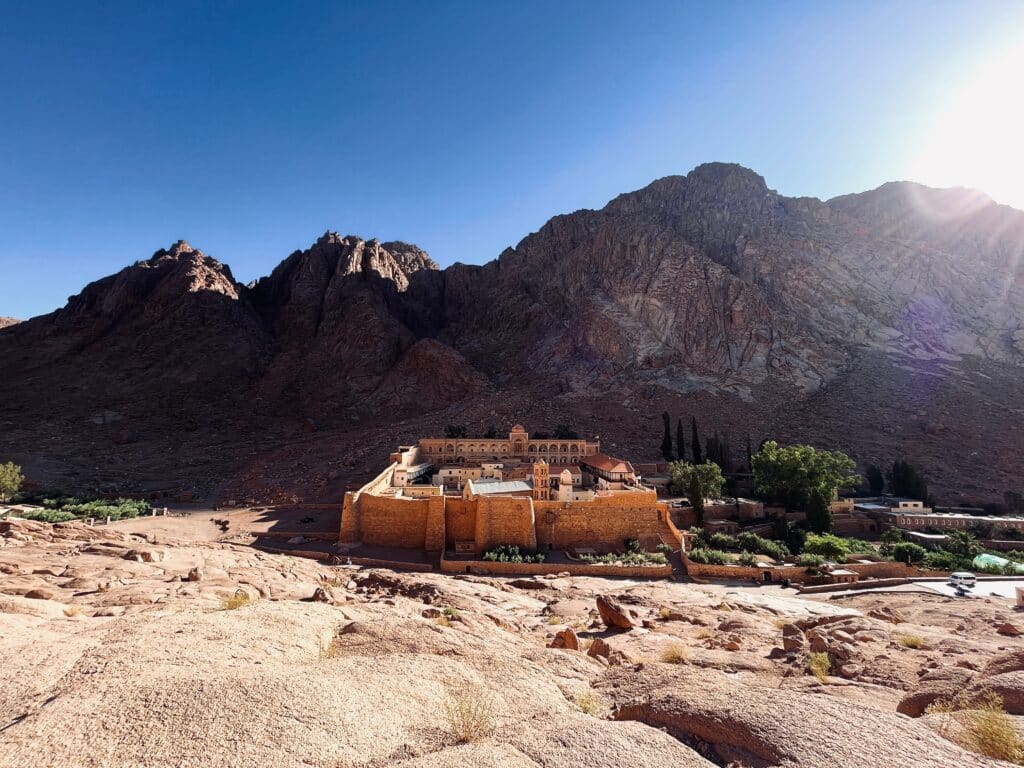 Panoramic view of Saint Catherine Monastery during sunset, framed by the dramatic peaks of the Sinai desert, a major pilgrimage destination.