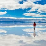 Girl in red on Salar de Uyuni in Bolivia covered with water with cloudy sky reflections