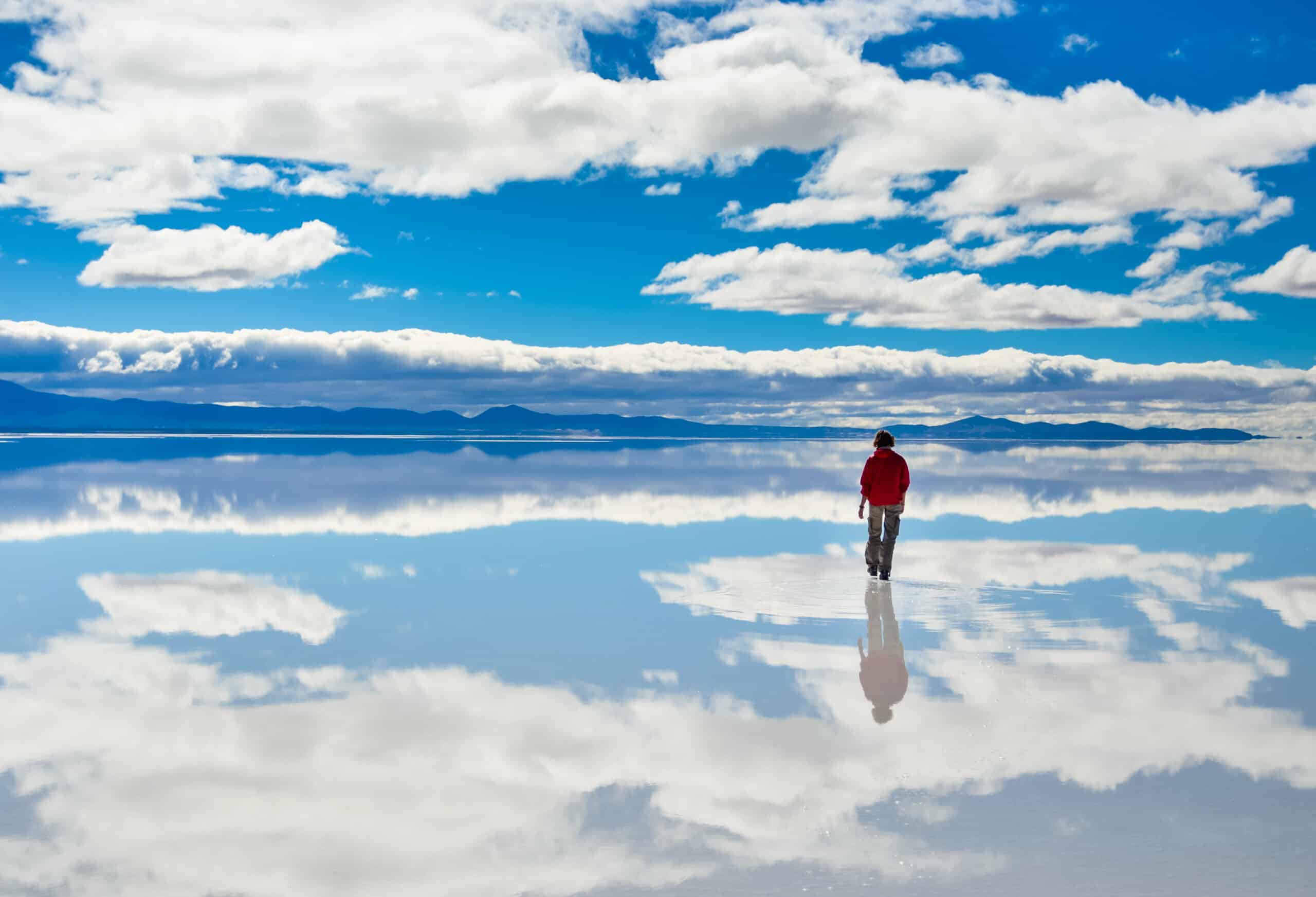 Girl in red on Salar de Uyuni in Bolivia covered with water with cloudy sky reflections