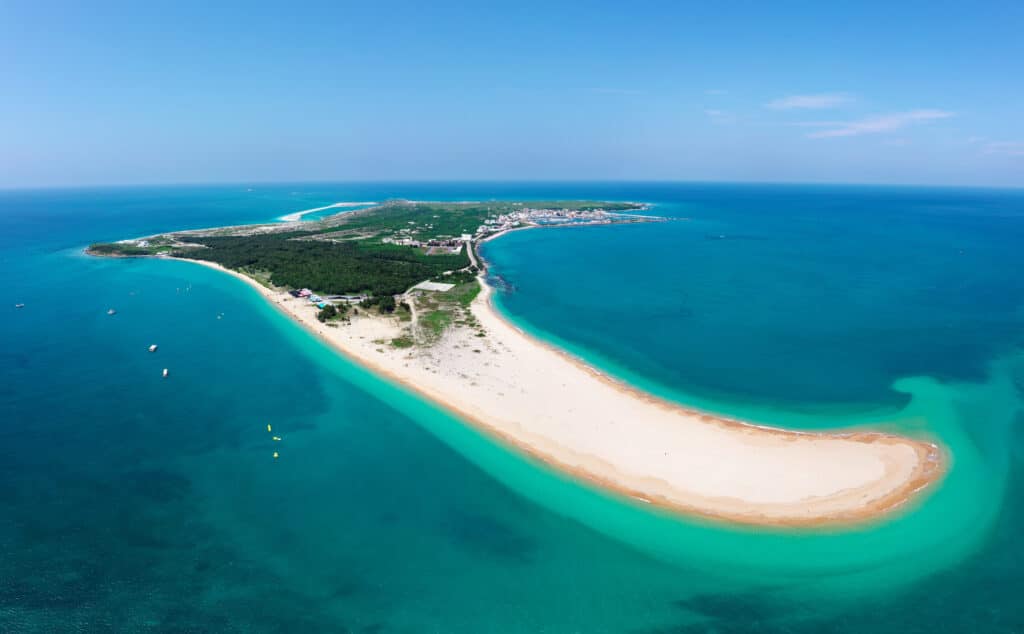 Aerial view of Jibei Island, a famous tourist destination for water sports in Baisha, Penghu County, Taiwan, with a beautiful sandspit extruding into the turquoise seawater under blue clear summer sky