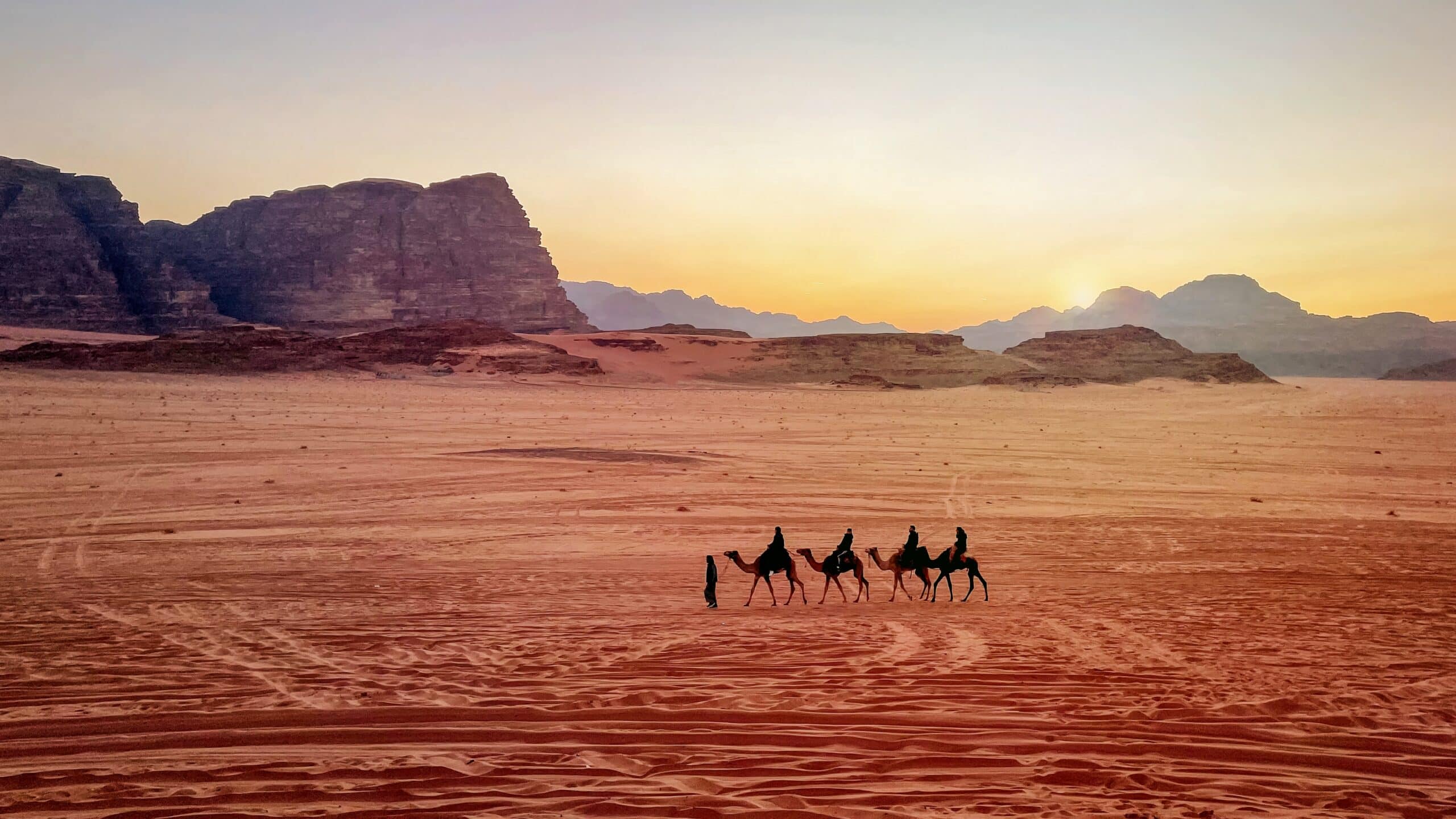 Jordan, Wadi Rum. Caravan of camels with drovers in the desert, rock mountains at sunset.