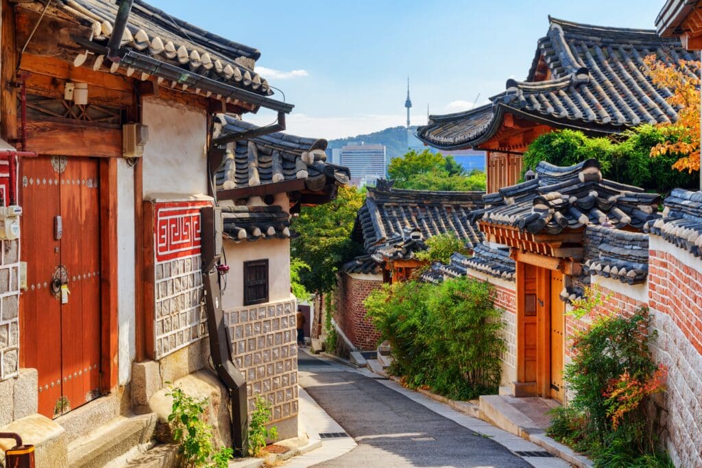 Gorgeous view of cozy old narrow street and traditional Korean houses of Bukchon Hanok Village in Seoul, South Korea. Seoul Tower on Namsan Mountain is visible on blue sky background. Scenic cityscape