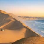 Car in the sand dunes and ocean view in Sandwich Harbour, Namib Naukluft Natural Park landscape in Namibia, Africa