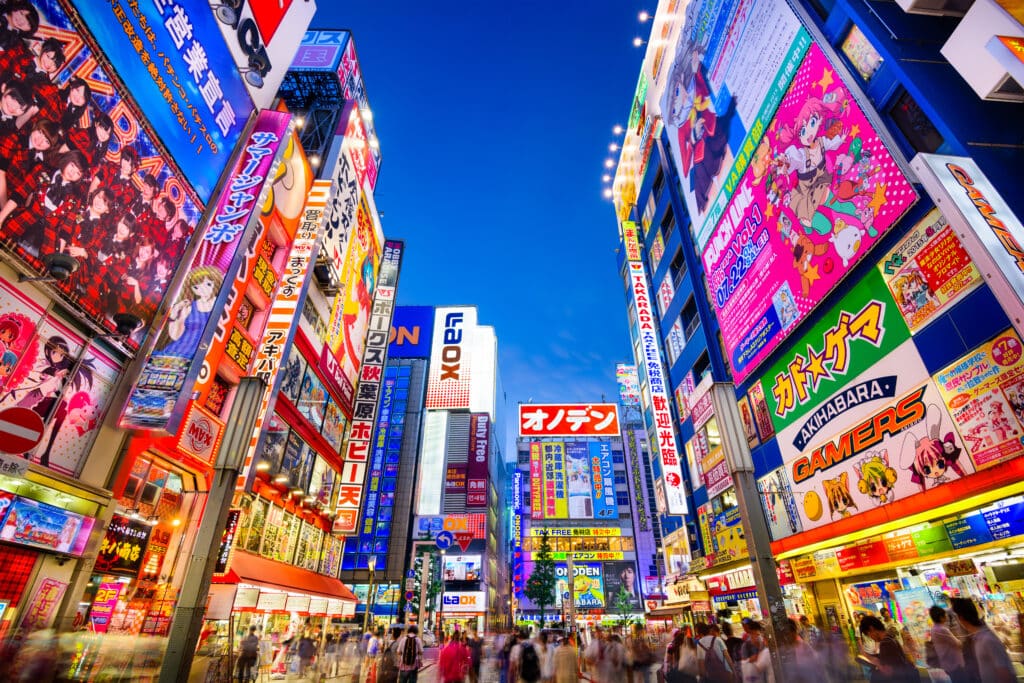 TOKYO, JAPAN: Crowds pass below colorful signs in Akihabara. The historic electronics district has evolved into a shopping area for video games, anime, manga, and computer goods.