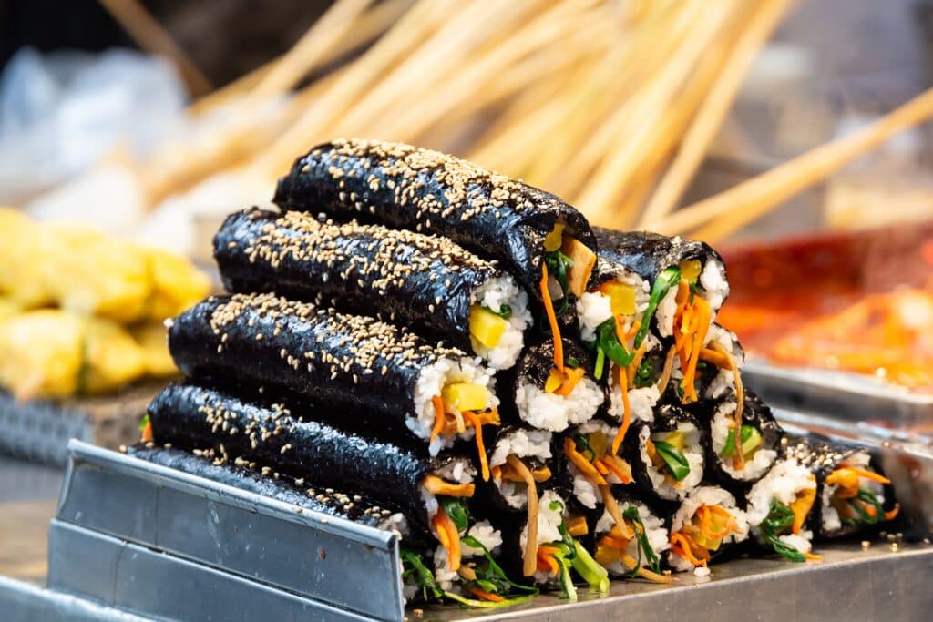 Korean gimbap rice rolls with vegetables and sesame seeds displayed at a street food stall