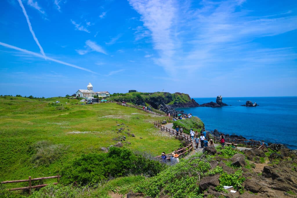 People relaxed walking on walkway close to the black beach or cliff from Volcanic rocks with blue sky and ocean at seopjikoji cape, Jeju isand, South korea.