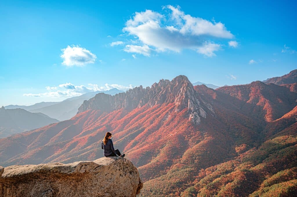 A young woman sits enjoying the beautiful autumn scenery on the Ulsanbawi rock cliff in the Sorossan Mountains near Goseong-gun, Gangwon-do Province. South Korea