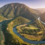 Aerial view of a Western Morava winding river snaking through a picturesque Ovcar Kablar valley, surrounded by lush green mountains in Serbia