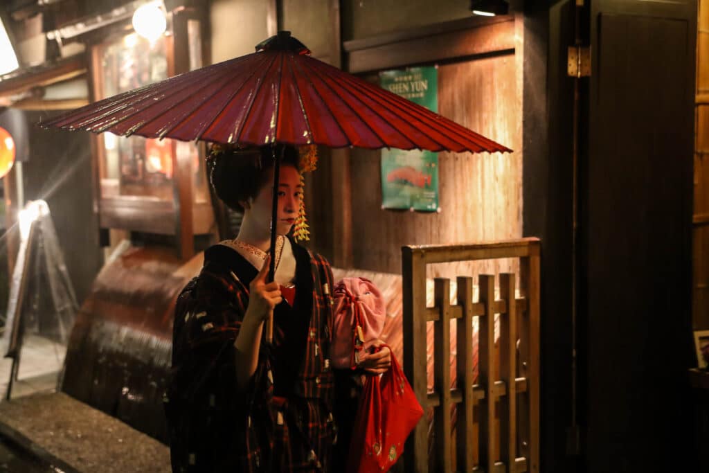 Maiko walking in Gion Kyoto at night with traditional umbrella