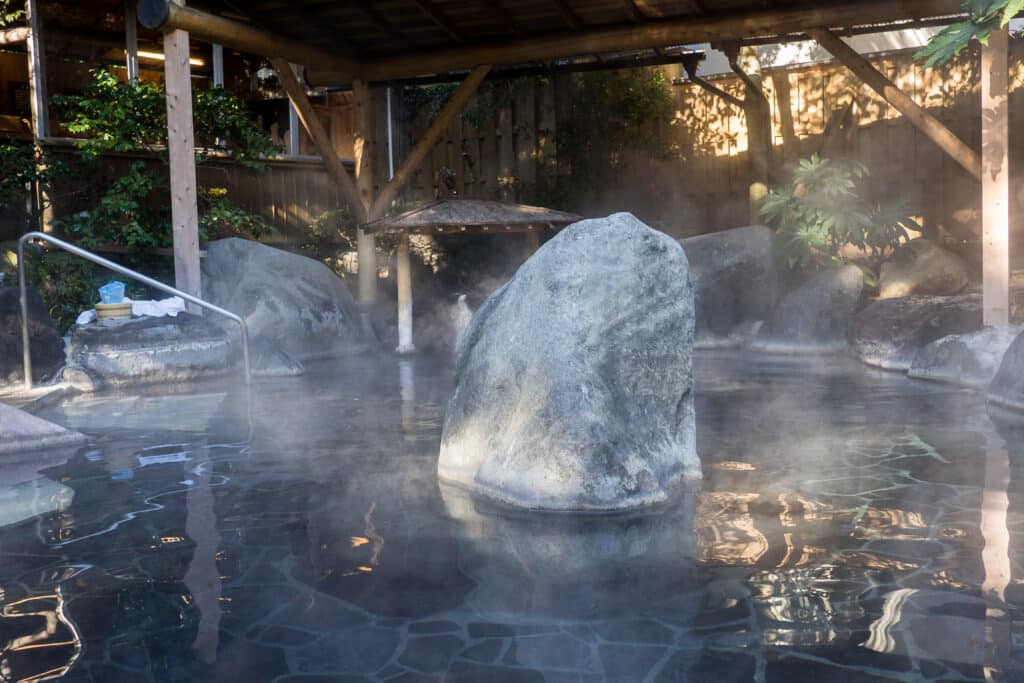 Outdoor onsen hot spring bath in Hakone with steam rising around natural rocks