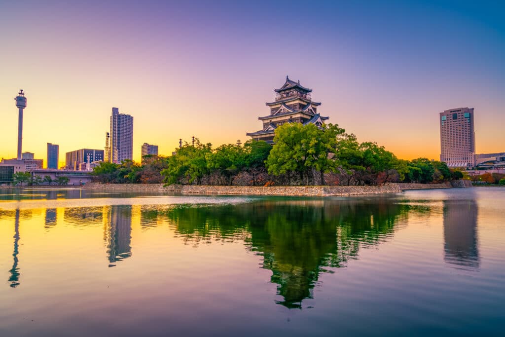 Hiroshima Castle at sunset reflected in the surrounding moat with city skyline