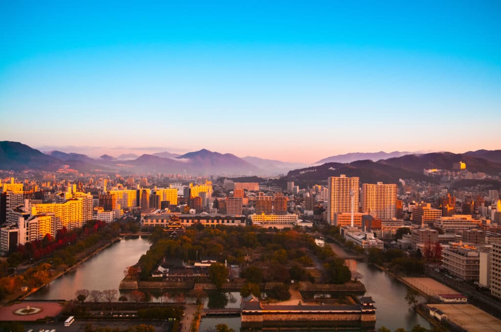 Aerial view of Hiroshima city skyline at sunset with surrounding mountains