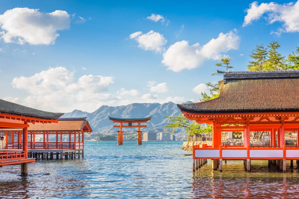 Itsukushima Shrine torii gate on Miyajima Island with traditional buildings over the water and mountains in the background