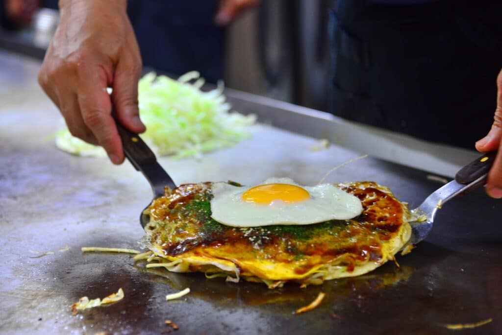 Hiroshima-style okonomiyaki being prepared on a teppan grill