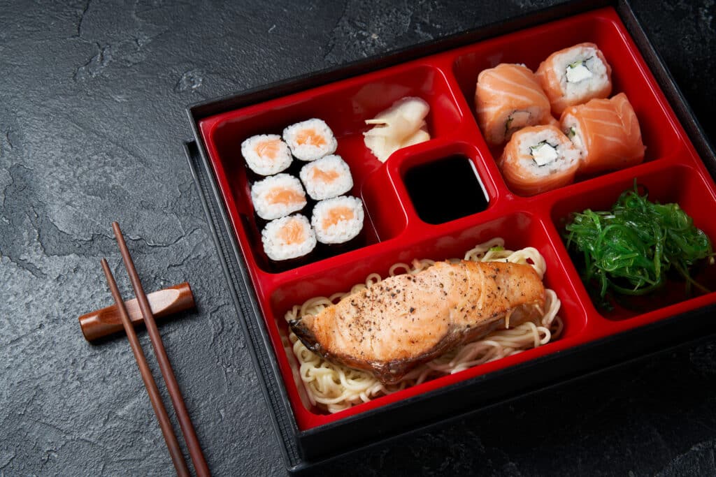 Japanese bento box with salmon sushi noodles and seaweed salad