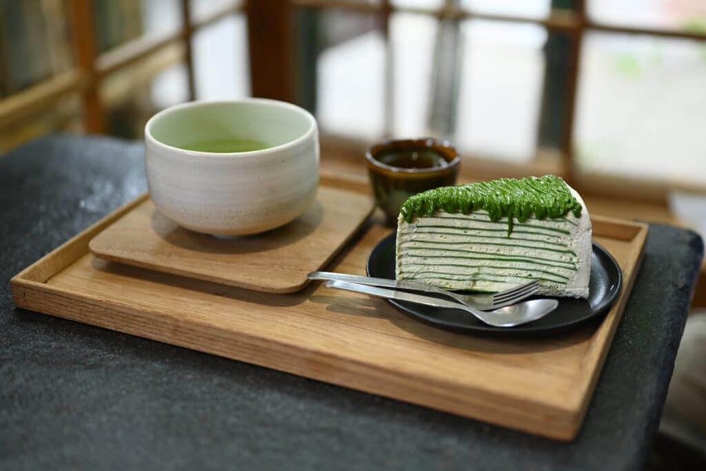 Matcha green tea with layered matcha cake on wooden tray