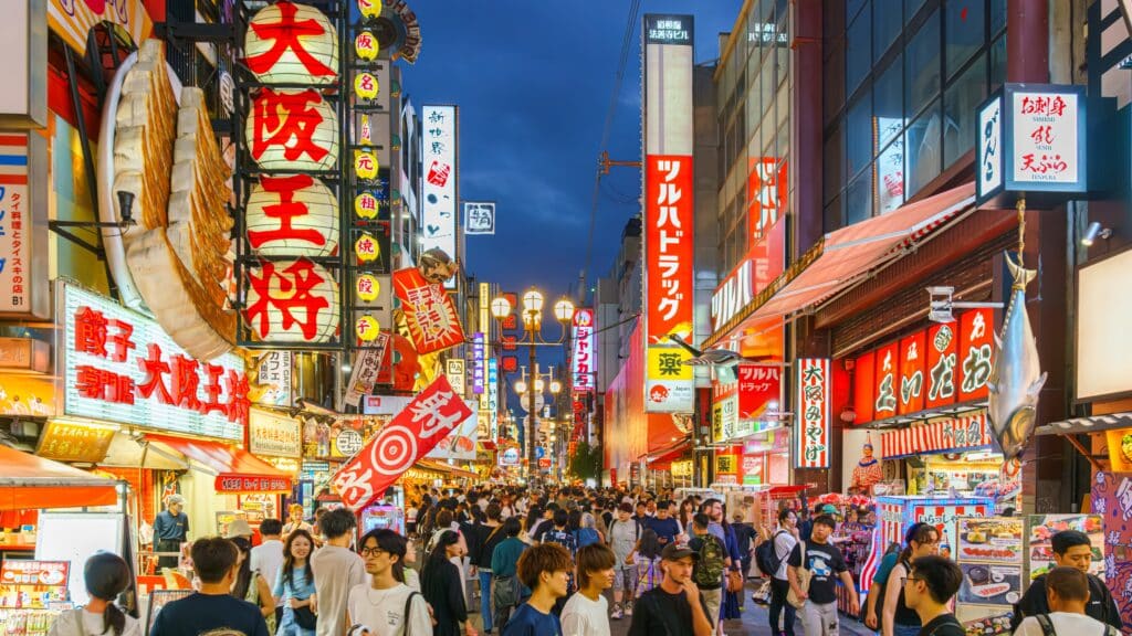 Crowded Dotonbori street in Osaka at night with neon signs and street food stalls