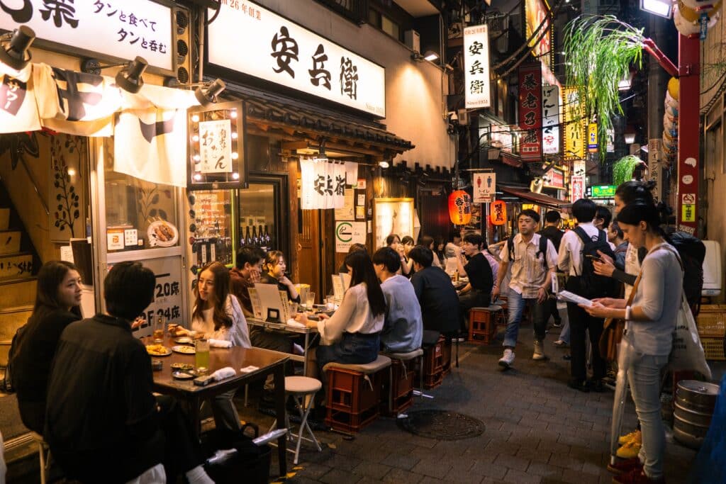 People dining at izakaya restaurants on a lively street at night in Shinjuku Tokyo Japan