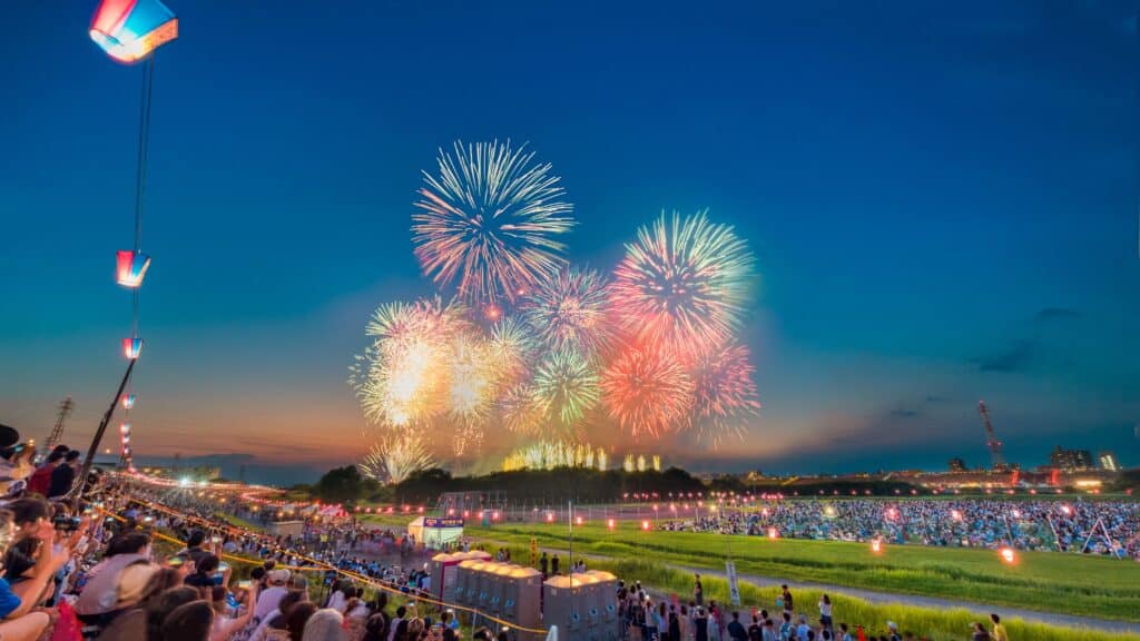 Large summer fireworks festival in Japan at dusk with crowds watching from the riverside