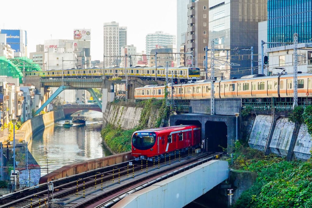 Multiple trains passing through a dense urban area in Tokyo beside a canal