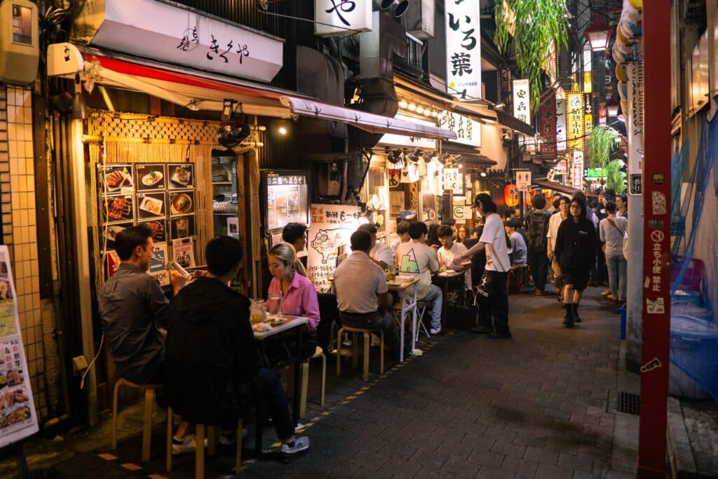 Narrow izakaya alley in Tokyo at night with diners seated outside small restaurants