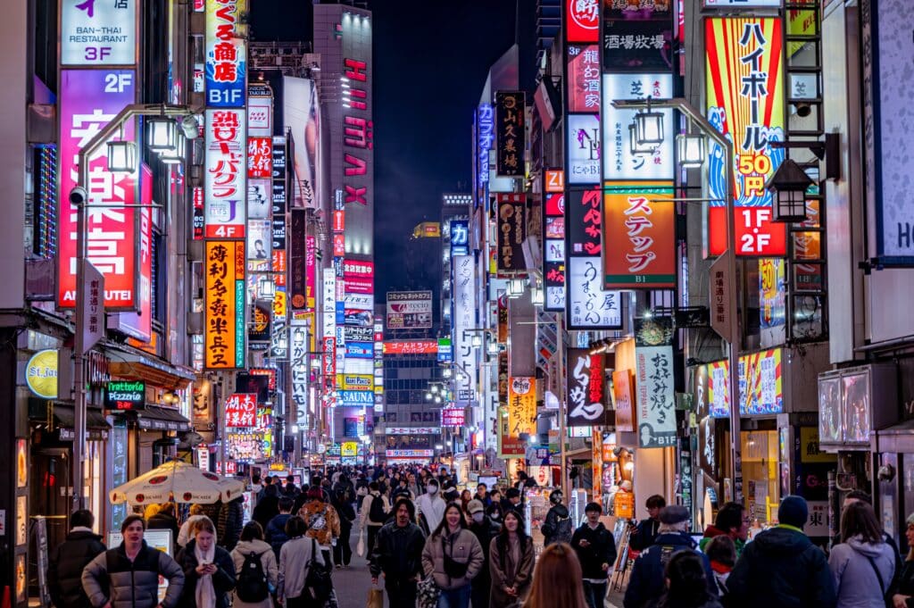Busy neon-lit street in Shinjuku at night with restaurants, signs, and crowds