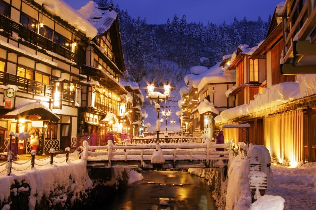 Snow-covered traditional hot spring town in Japan illuminated at dusk during winter