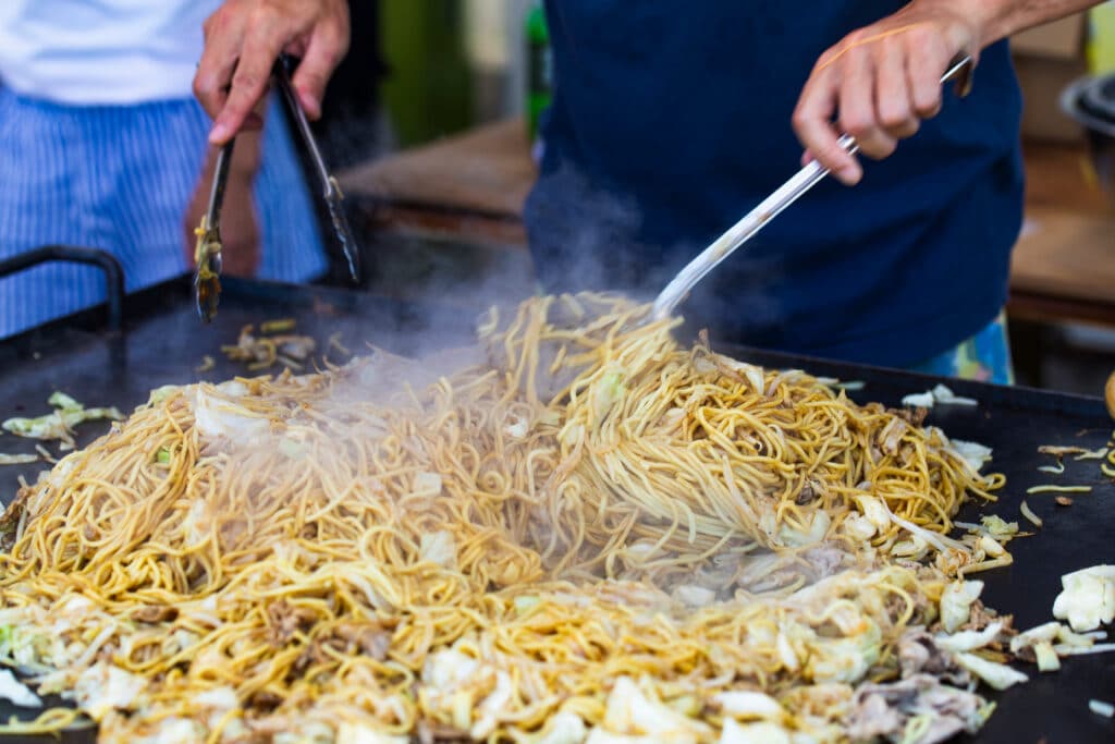 Yakisoba noodles cooking on a large Japanese street food grill