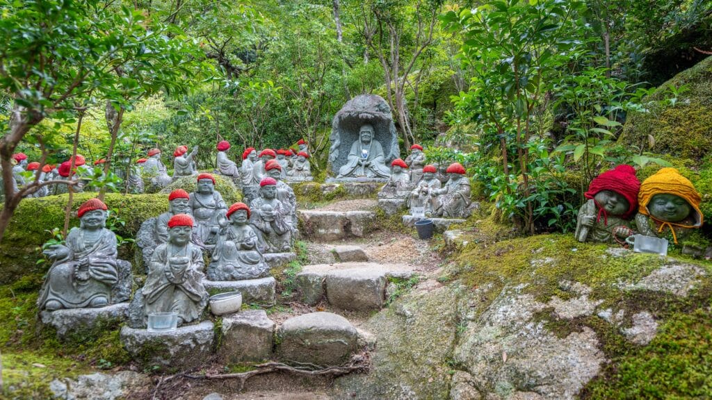 Stone Buddhist statues surrounded by moss and greenery at Daisho-in Temple on Miyajima