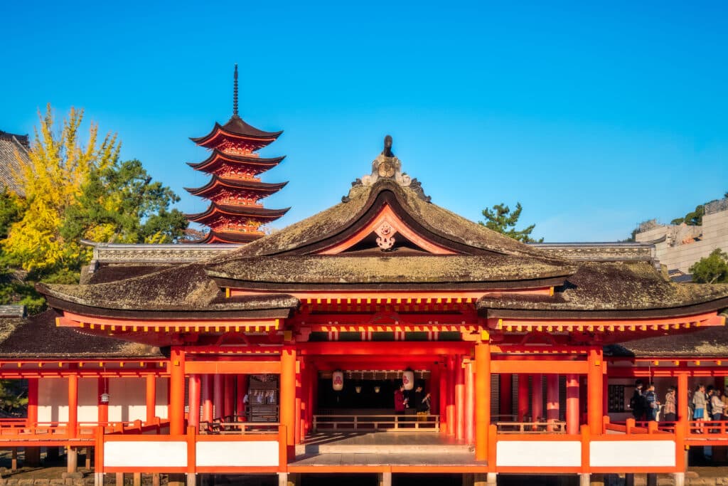 Vermilion buildings of Itsukushima Shrine with the Five-Story Pagoda rising behind them on Miyajima