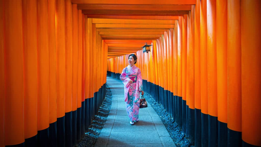 Woman in kimono walking through the red torii gates of Fushimi Inari Shrine in Kyoto