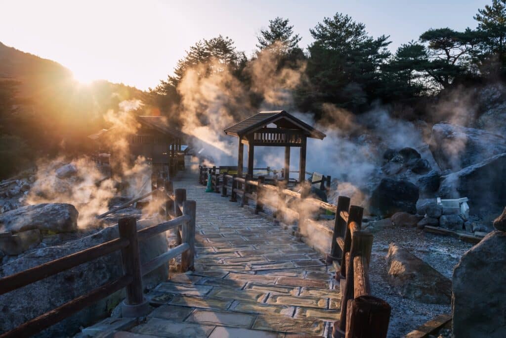 Steam rising from a traditional Japanese onsen area with wooden walkways and morning sunlight
