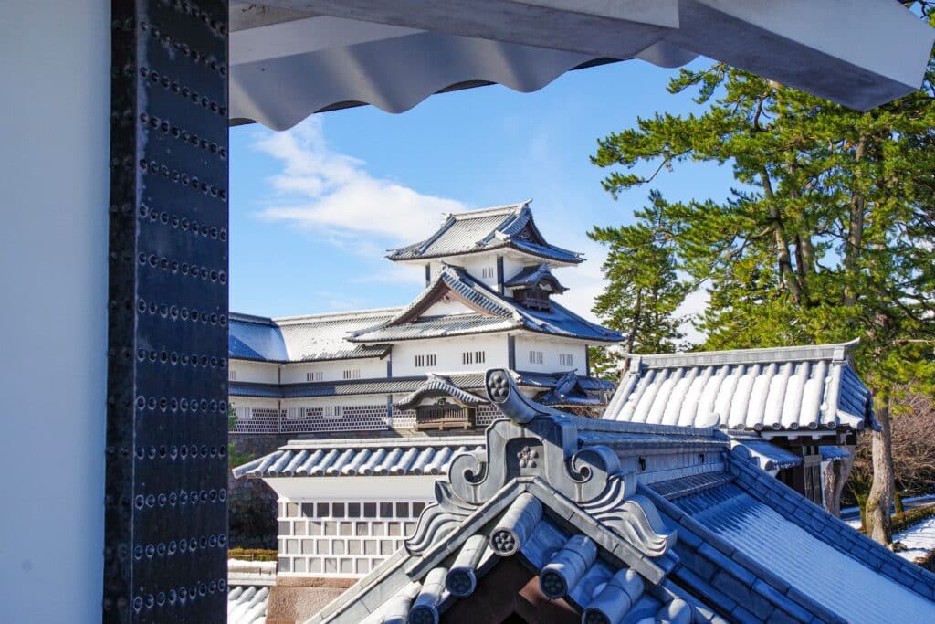 Snow-covered rooftops and Kanazawa Castle viewed through a traditional gate
