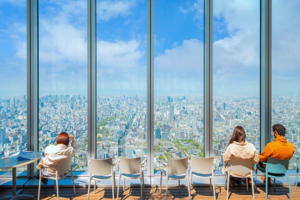 View over Osaka skyline from Abeno Harukas observation deck with visitors sitting by large windows